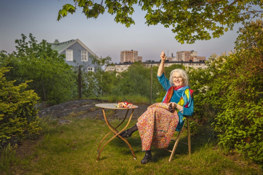 Elisabeth Skoglund sitter i en trädgård och broderar sitt evighetsbroderi.