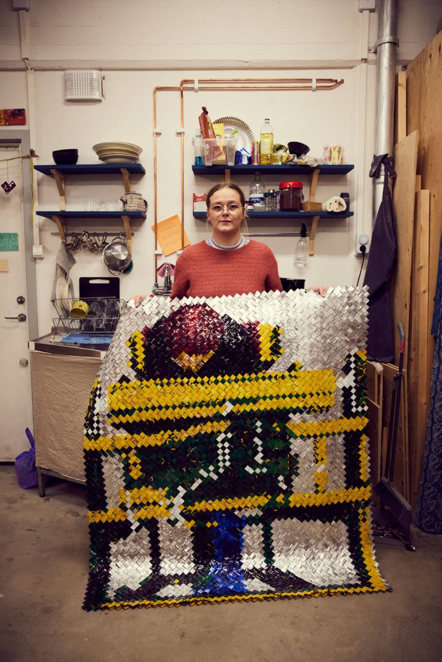 Lisa Juntunen Roos håller upp en bild uppbyggd av flätade remsor från kaffepaket.