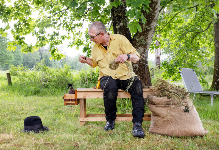 Michael Ritter sitter på en bänk och flätar en korg av gräs.