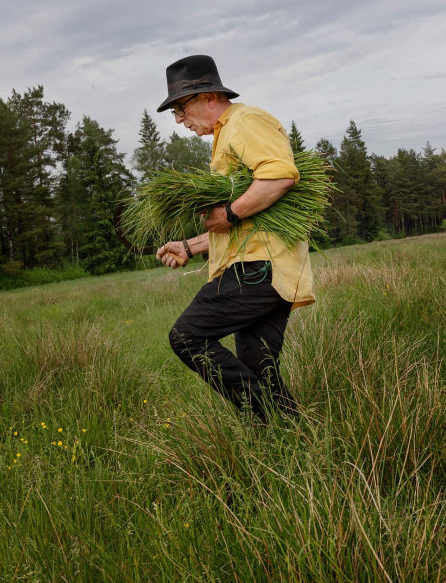 Michael Ritter går på en äng med ett stort knippe gräs under armen.