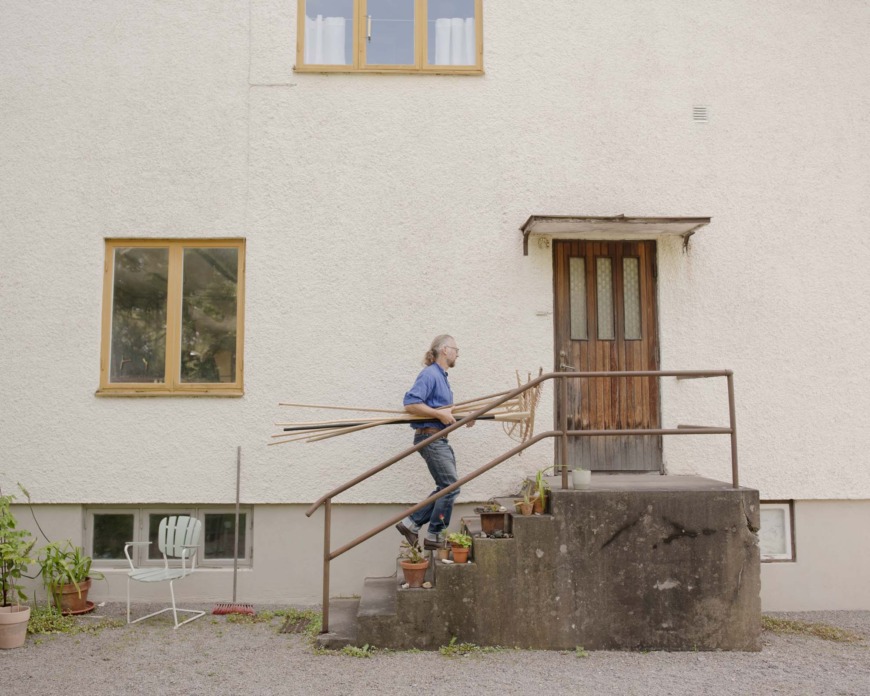 Martin Ericsson går upp för en trapp med flera räfsor i famnen.