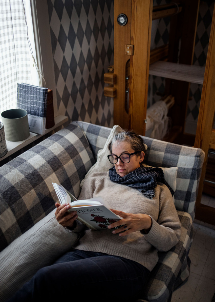 Åsa Pärson ligger och läser på en soffa med blå- och vitrutigt tyg.