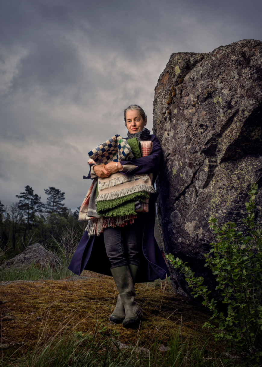 Åsa Pärson står lutad mot en stenbumling med famnen full av textilier.